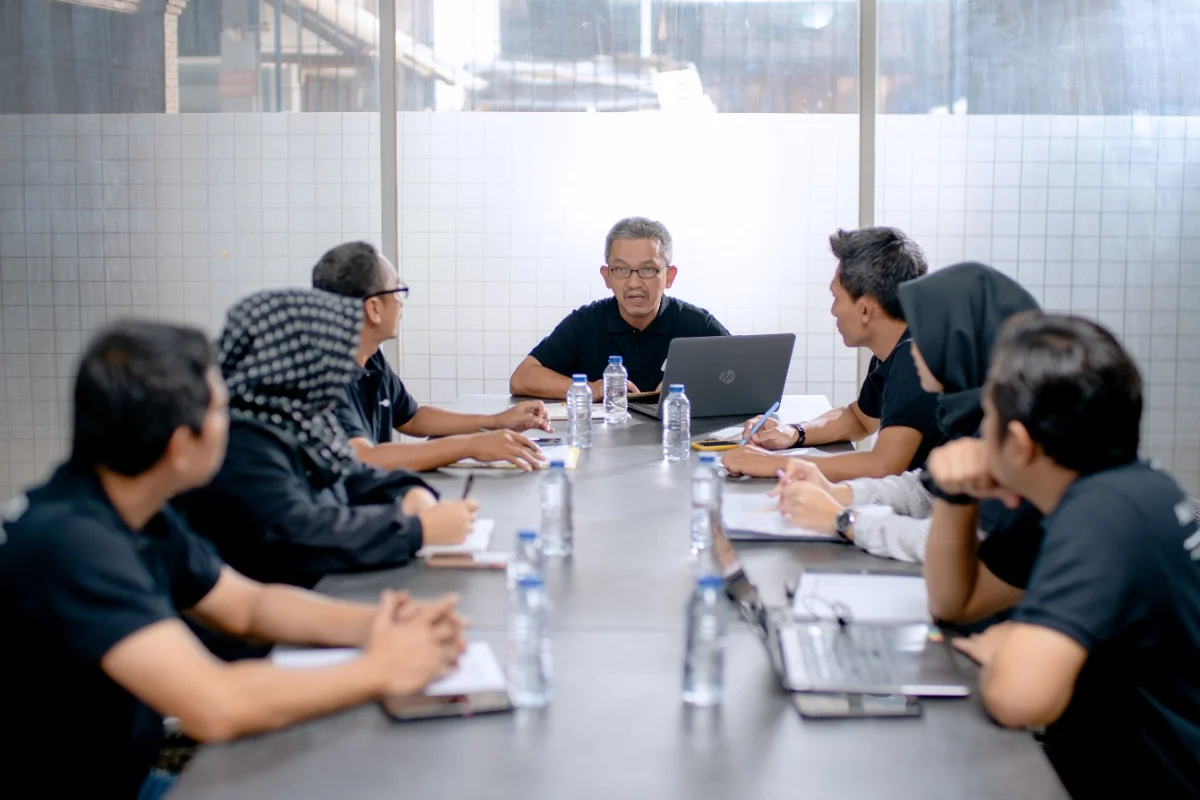 Project team around a meeting table with laptops and printed registers.